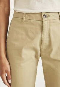 Pantaloni in cotone beige leggeri con vestibilità dritta, dotati di una chiusura con bottone argentato e dettagli di cucitura discreti lungo le cuciture.