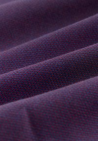 Teksturowana tkanina w głębokim niebieskim kolorze z geometrycznym wzorem z małymi czerwonymi akcentami, tworzącymi subtelny efekt trójwymiarowy.