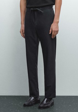 Pantaloni neri a sigaretta con vita a lacci, texture liscia, tasche laterali e vestibilità sartoriale, abbinati a mocassini neri.