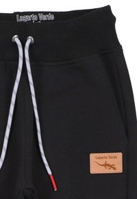 Schwarze Sweatpants mit elastischem Bund, ausgestattet mit grauen Kordeln mit roten Enden und einem beigefarbenen Lederpatch mit der Aufschrift "Lagarto Verde."