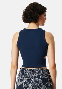 Navyblauw ribgebreid crop top met een ronde halslijn en een open zijdetail, gecombineerd met gestreepte pants met vredestekens en sterren.