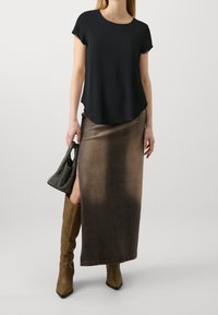 Haut noir à manches courtes associé à une jupe longue dégradée marron, bottes marron texturées montant jusqu'aux genoux, et un sac à main noir perforé.