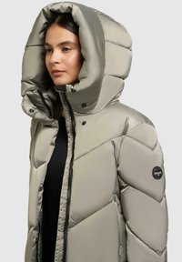Pufferjacke in Hellgrau mit einer großen, gesteppten Kapuze. Verfügt über Druckknöpfe und ein Logo-Patch am Ärmel. Glatte, glänzende Oberfläche.