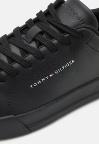Sneaker in pelle nera con lacci tondi neri, superficie testurizzata e logo "TOMMY HILFIGER" bianco con un accento colorato sul lato.