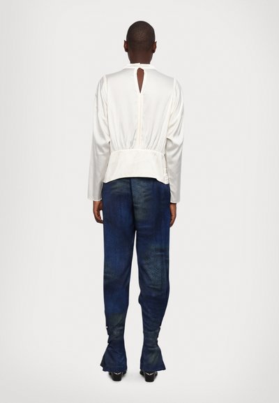 Vit satin långärmad topp med en nyckelhålsöppning i ryggen, kombinerad med blå denimbyxor med utsvängd fåll och kontrasterande textur.
