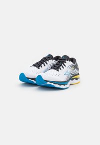 Zapatillas de running con una parte superior de malla blanca y acentos negros, detalles en azul y amarillo, suela texturizada, y puntera reforzada.
