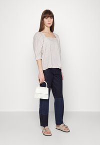 Blusa riscada com mangas bufantes, combinada com calças de ganga em blocos de cores. Modelo segura uma bolsa branca com textura de crocodilo e uma alça estruturada.