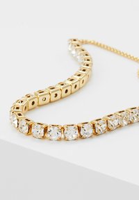 Zelta tonī veidota kaklarota ar kvadrātveida posmiem un caurspīdīgiem kristāla akcentiem, ar elegantu dizainu un gludu virsmu.