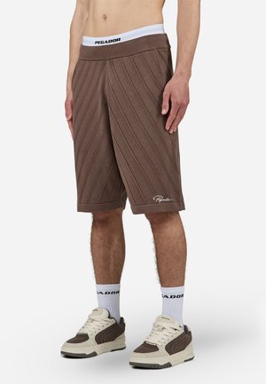 Brown knitted shorts with diagonal ribbed texture, elastic waistband featuring "PEGADOR," and a white logo at the hem.