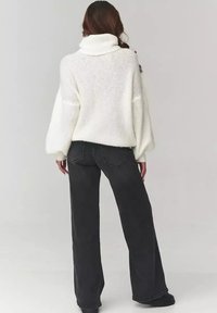 Biały, gruby sweter z wysokim kołnierzem i rękawami typu balon, zestawiony z wysokim stanem, ciemnoszarymi spodniami o szerokich nogawkach.