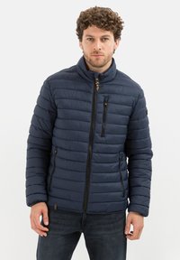 Marineblauwe pufferjack met horizontale stiksels, hoge kraag, ritszakken en elastische manchetten. Gemaakt van lichtgewicht, waterafstotend materiaal.