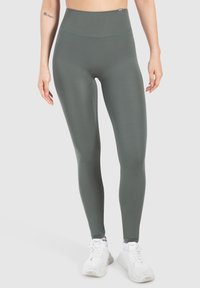Legginsy z wysokim stanem i dopasowanym krojem w stonowanym zielonym kolorze, wykonane z elastycznego materiału. Posiadają gładką teksturę i subtelne detale szwów.