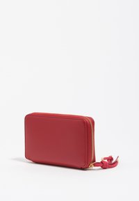 Cartera de cuero rojo con forma rectangular, cierre de cremallera dorada y un acento de nudo en el tirador de la cremallera. Textura suave, diseño minimalista.