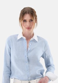 Light blue striped button-up shirt with a white collar and cuffs. Features a relaxed fit and textured fabric with vertical stripes.