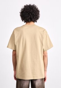 Bežinė trumpa rankovė t-shirt pagaminta iš medvilnės. Savybėms būdingas laisvas siluetas, apvalus kaklas ir minimalūs siuvimo elementai.