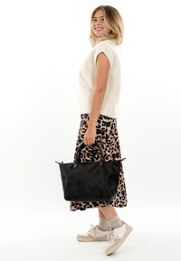 Zwarte draagtas met afgeronde handvatten, slank ontwerp, gemaakt van gestructureerde stof. Gecombineerd met een wit bovenstuk en een rok met luipaardprint, gecombineerd met sneakers.