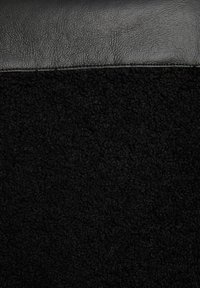 Pelle nera e tessuto in pile nero texture, accostati, con una sezione superiore liscia e una sezione inferiore morbida e soffice.