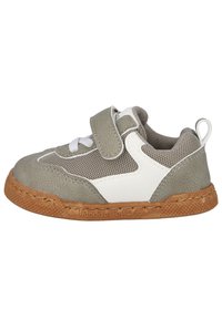 Zapatilla gris y blanca con tela de malla, suela de goma y correa de Velcro. Presenta un upper texturizado y costuras decorativas. Marca grabada en la suela.