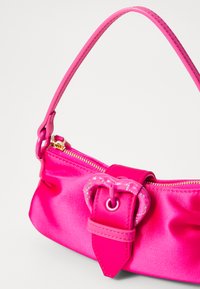 Ροζ σατέν τσάντα χειρός με δομημένο σχήμα, διαθέτει αγκράφα σε σχήμα καρδιάς και κλείσιμο με φερμουάρ. Λείος υφής και ρυθμιζόμενη λαβή.
