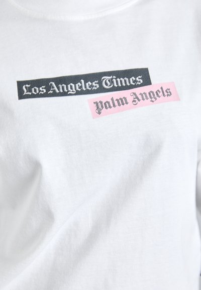 White cotton t-shirt featuring bold printed text: "Los Angeles Times" in black and "Palm Angels" in pink, both on contrasting rectangular blocks.