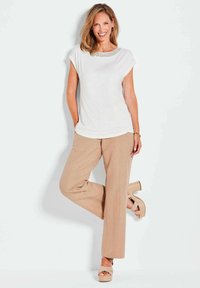 Weißes Kurzarmoberteil mit strukturiertem Ausschnitt, kombiniert mit beigen weit geschnittenen Hosen und hellbraunen Absatzsandalen mit Riemchen-Design.