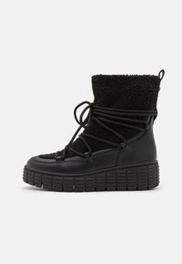 Botas negras con un material de pelo texturizado en la parte superior, punta redonda y una suela de goma gruesa con detalles estriados. Aseguradas con cordones en la parte delantera.