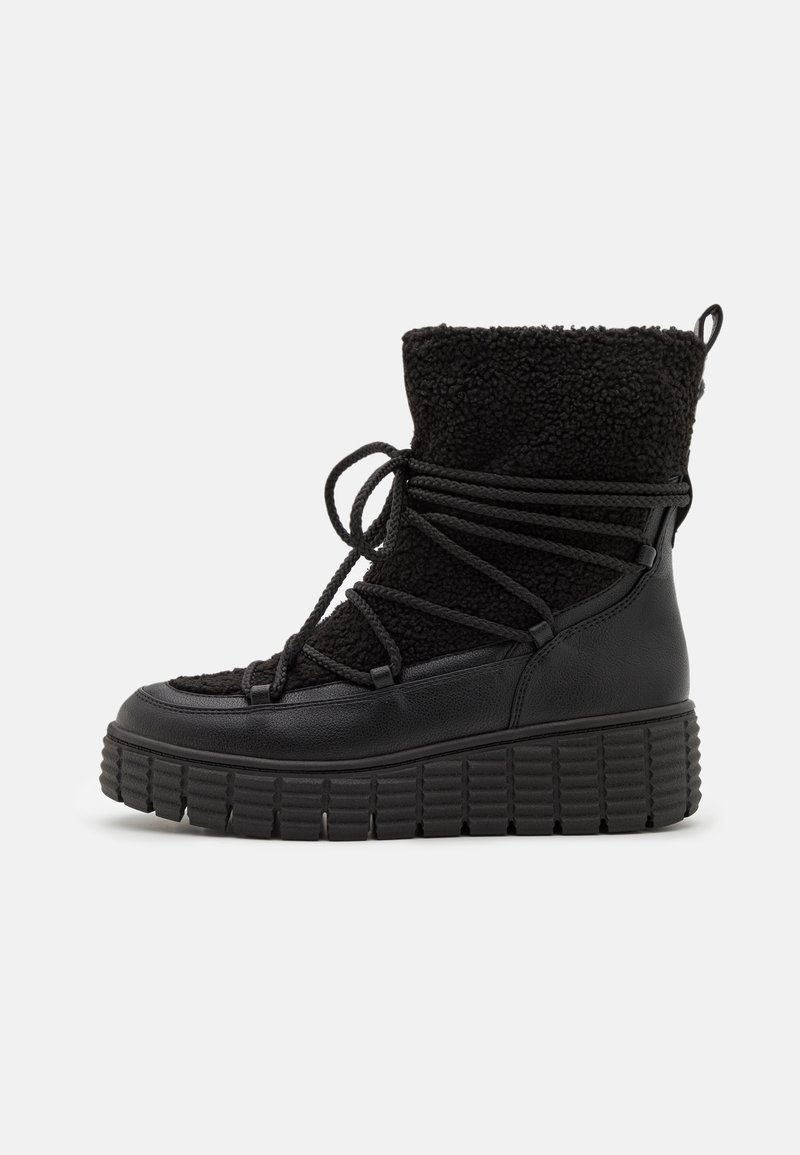 Botas negras con un material de pelo texturizado en la parte superior, punta redonda y una suela de goma gruesa con detalles estriados. Aseguradas con cordones en la parte delantera.