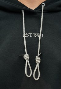 Μαύρο φούτερ με κουκούλα με την επιγραφή "EST.1981" σε λευκό κείμενο. Ασημί κορδόνια με υφή και μαύρα πλαστικά άκρα.