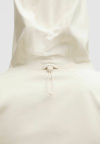 Lightweight cream-colored hooded jacket featuring a drawstring adjustment at the back and a smooth, textured surface.