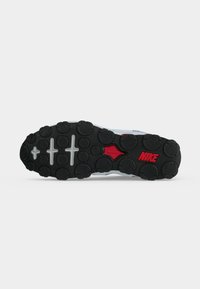 Μαύρη λαστιχένια σόλα ενός παπουτσιού Nike με κυκλικά σχέδια πέλματος και κόκκινο λογότυπο Nike κοντά στην περιοχή της καμάρας σε λευκό φόντο.