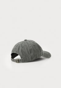 Cappellino grigio in cotone con visiera pre-curvata, cinturino regolabile e texture leggermente sbiadita. Presenta fori di ventilazione e pulsante sopra cucito.