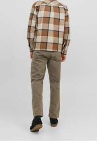 Bruine en crèmekleurige geruite flanellen overhemd, met de manchet los, gecombineerd met tan kleurige katoenen broek en zwarte suède schoenen, bekeken van achteren.