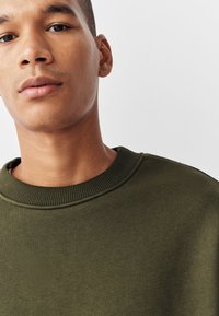 Olivgrön sweatshirt i slät tyg med ribbad rund halsringning och avslappnad passform. Inga synliga mönster eller detaljer.