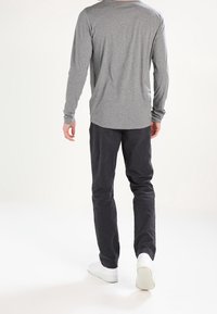 Gray long-sleeve shirt, relaxed fit; paired with dark pants and white sneakers; smooth texture and simple design visible from the back.