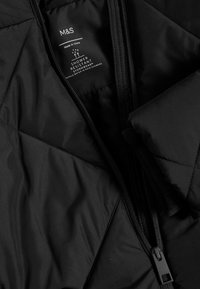 Giacca nera trapuntata con chiusura a zip, etichetta resistente all'acqua e texture liscia. Include elementi di design stormwear e hardware nero.