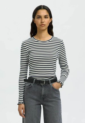 Langermet stripete strikket topp i marineblått og hvitt med en ribbestrikket tekstur. Har rund halslinning og subtile bølgekantede mansjetter. Brukt med høy påsydde grå jeans.