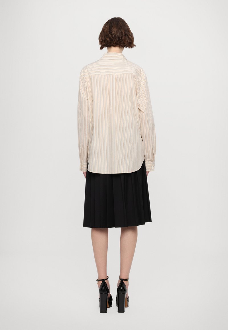 Camisa de cuello en tejido ligero con rayas verticales en colores pastel. Combinada con una falda negra con pliegues y zapatos de tacón alto negros.