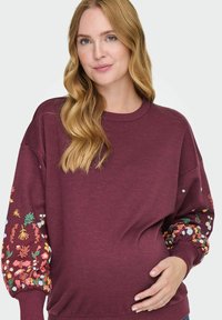 Felpa bordeaux con ricami floreali sulle maniche, scollo e polsini a coste, vestibilità rilassata e una texture morbida. Adatta per l'abbigliamento maternità.