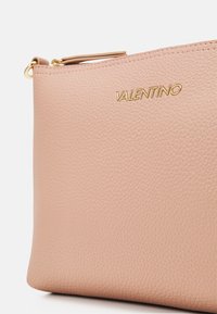 Rožinė odinė piniginė su tekstūruota paviršiumi ir auksiniu "Valentino" logotipu. Įeina užtrauktukas ir mažas odinis laikiklis.