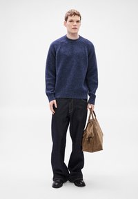 Μπλε σκούρο πλεκτό πουλόβερ με μακριά μανίκια και λαιμόκοψη στρογγυλή, συνδυασμένο με σκούρο τζιν παντελόνι και καφέ δερμάτινη τσάντα. Λείο ύφασμα.