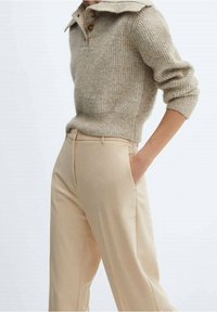 Beige geribbelde trui met een kraaglijn en drie knopen, gecombineerd met lichtbeige op maat gemaakte broek met zijzakken.
