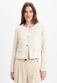 Crème cropped jack gemaakt van textuurstof, met zilveren knopen en twee voorkoppelzakken, gecombineerd met beige hoge taille broek.