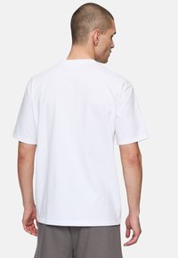 Camiseta de algodón blanca con mangas cortas, cuello redondo y un ajuste relajado, que presenta una textura suave y sin patrones ni gráficos visibles.