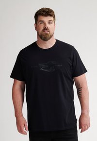 Camiseta de algodón negra con cuello redondo y un sutil gráfico de un coche con texto. Mangas cortas y corte relajado.