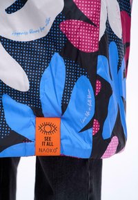 Barevná potištěná bunda s velkými modrými a růžovými květinovými vzory na černém pozadí. Obsahuje oranžovou štítek se značkou.