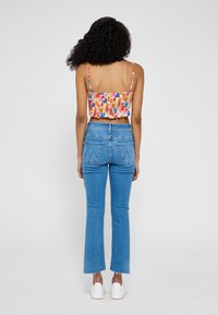 Top corto floreale con spalline sottili e orlo arricciato, abbinato a jeans flare a vita alta di colore azzurro chiaro con tasche posteriori e orlo grezzo.