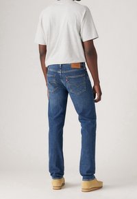 Light gray t-shirt, blue denim jeans with a textured finish, and tan shoes. Notable features include back pockets and a leather patch.