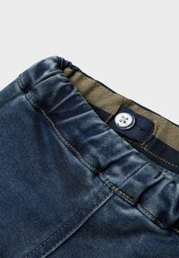 Denim hlače s elastiko v pasu, svetlo modre barve, diskretnimi šivi in kovinskim gumbom za zapiranje.