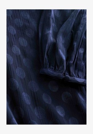 Bluză din țesătură navy blue cu buline mari, circulare. Material ușor, cu textură, cu mâneci bufante și detaliu cu nasture la manșetă.