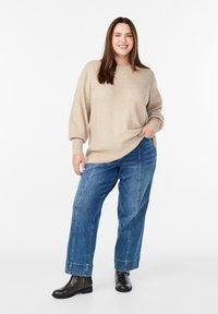 Beżowy sweter dzianinowy z okrągłym dekoltem i subtelnymi zdobieniami, połączony z niebieskimi spodniami o wysokim stanie i szerokimi nogawkami oraz czarnymi botkami na kostkę.